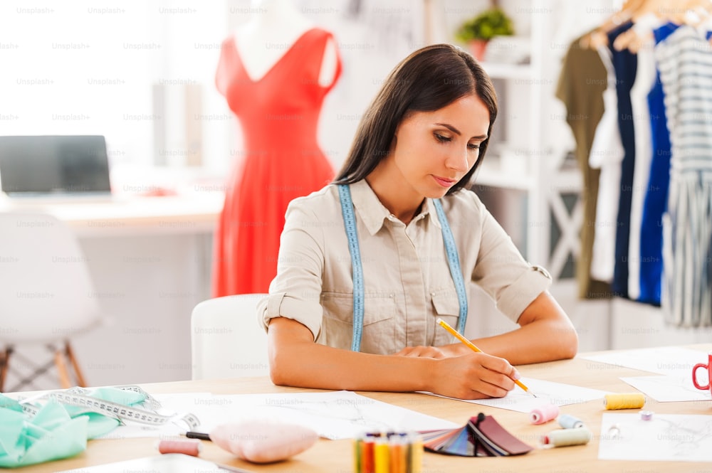 Dibujo de una joven seria mientras está sentada en su lugar de trabajo en el taller de moda