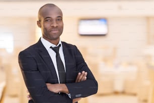 Cheerful young African man in full suit keeping arms crossed and looking at camera