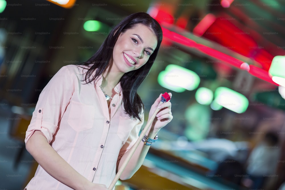 Young beautiful woman chalking the snooker cue and smiling in a club