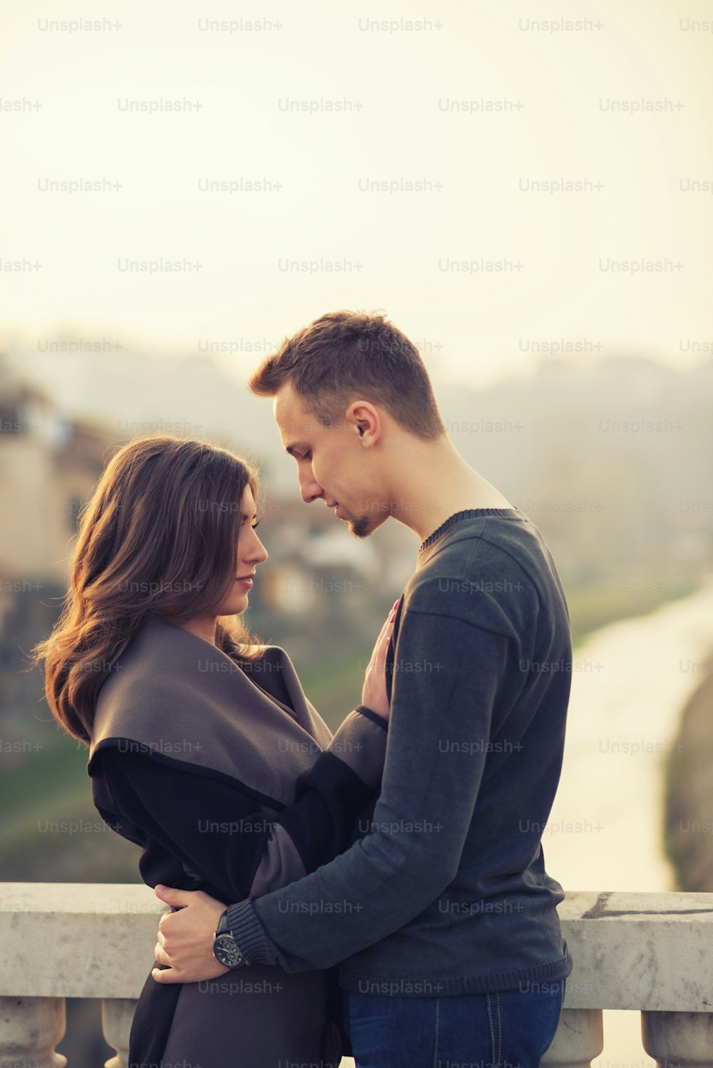 Handsome young couple standing on a bridge, hugging and enjoying the beautiful sunset.
