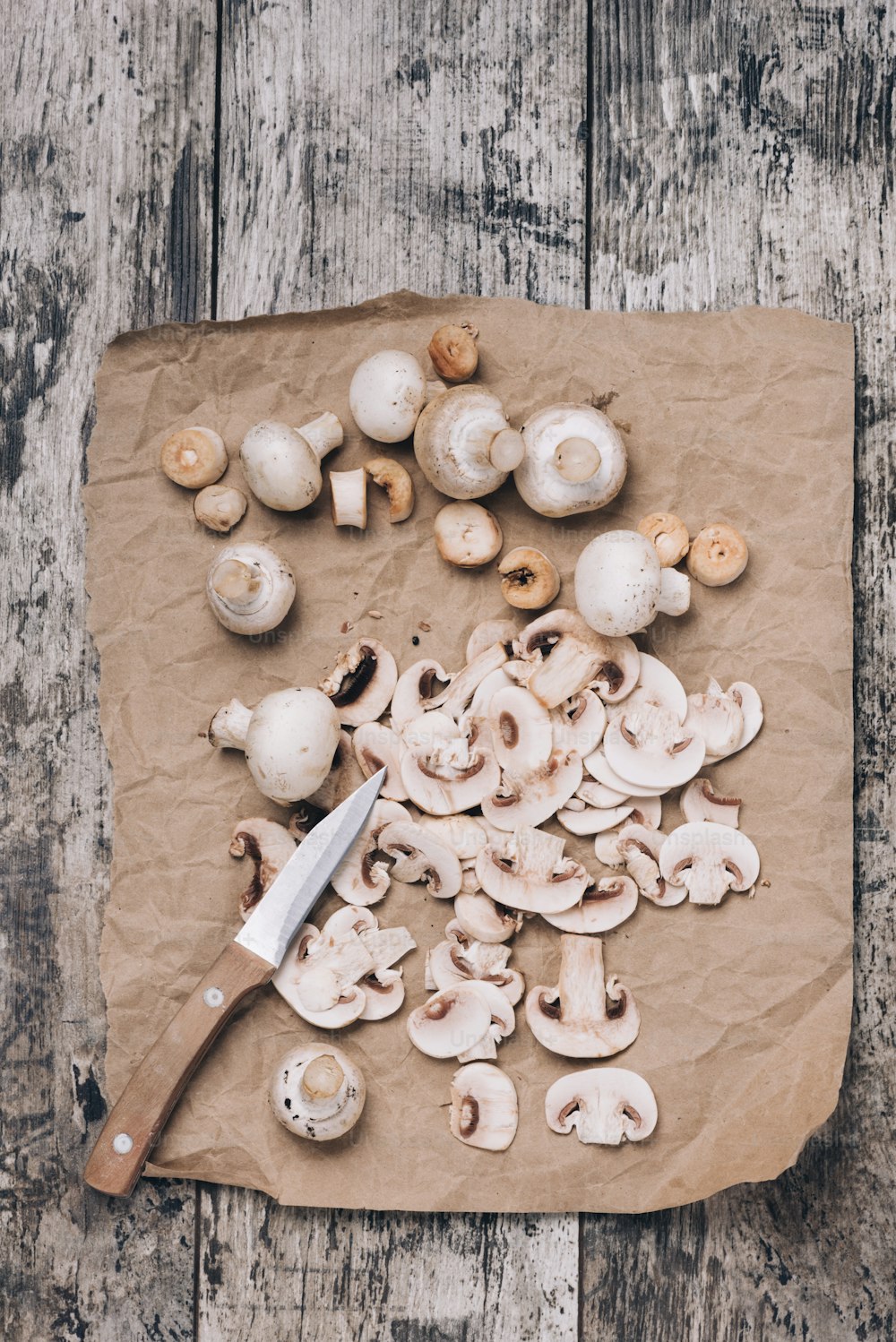 Funghi champignon freschi interi e affettati fotografati dall'alto su un vecchio tavolo di legno.