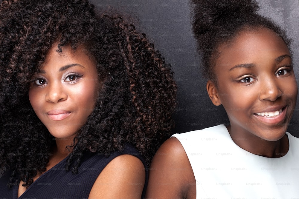 Duas lindas meninas afro-americanas sorrindo, olhando para a câmera. Irmãs posando com roupas elegantes. Foto de estúdio.