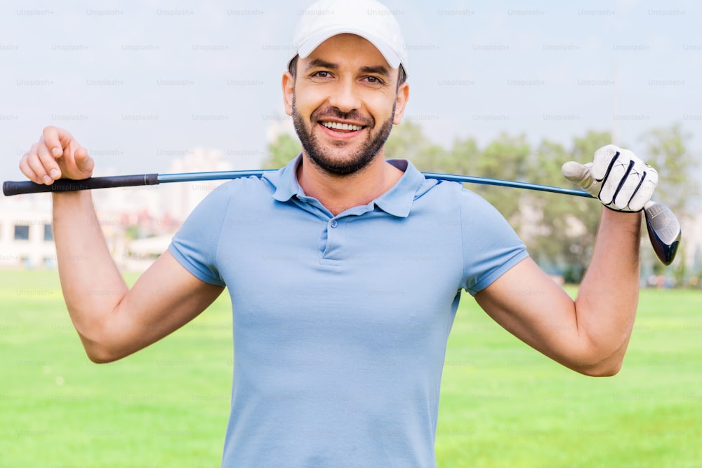Smiling young man carrying golf club on shoulders while standing on the golf course