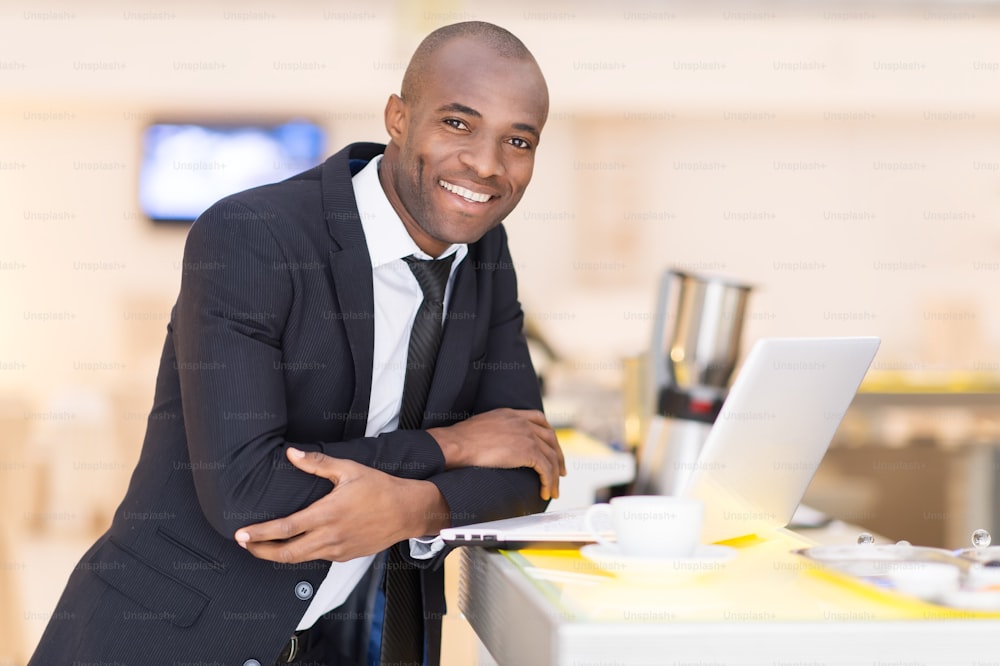 Cheerful young African man in formalwear using his laptop while leaning at bar