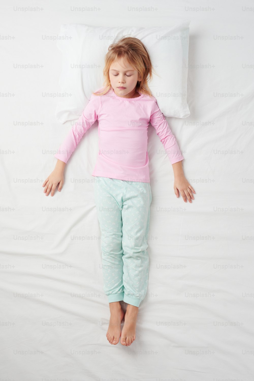 Top view photo of little girl sleeping on white bed. Quiet Soldier pose. Concept of sleeping poses