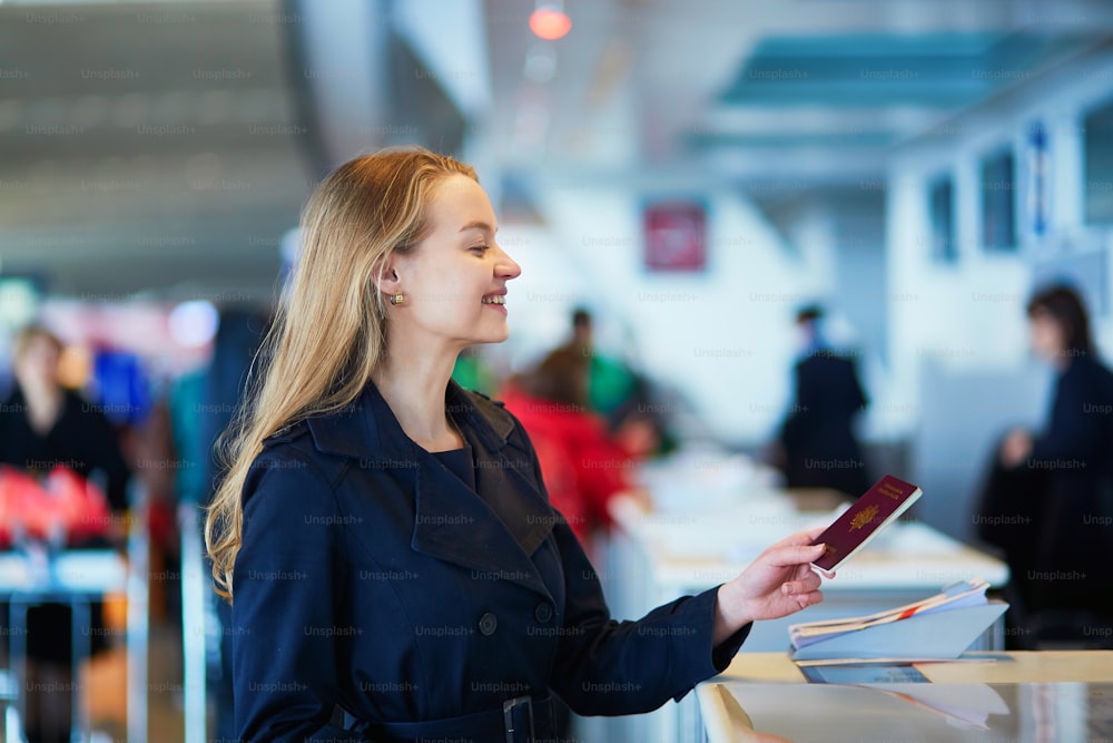 Young woman in international airport at check-in counter, giving her passport to an officer and waiting for her boarding pass