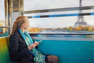 Bella giovane donna che viaggia in un treno della metropolitana parigina e usando il suo telefono cellulare. La torre Eiffel è dietro la finestra