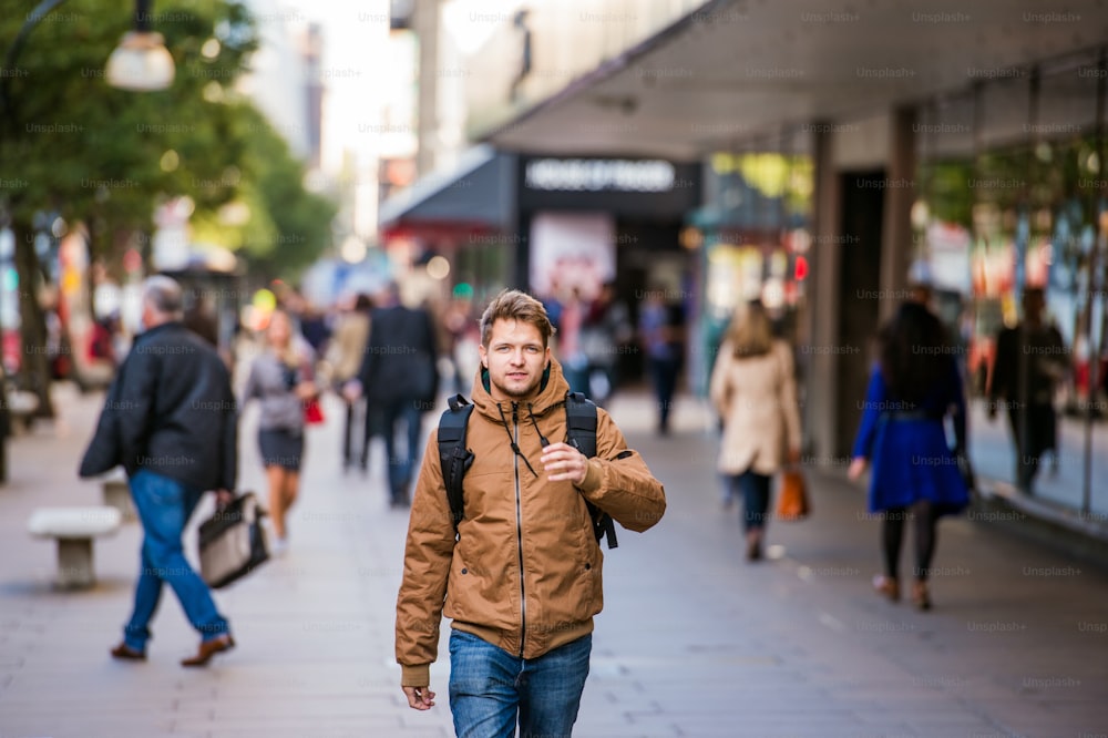 갈색 겨울 재킷을 입은 젊은 힙스터 남자가 런던의 거리를 걷고 있다