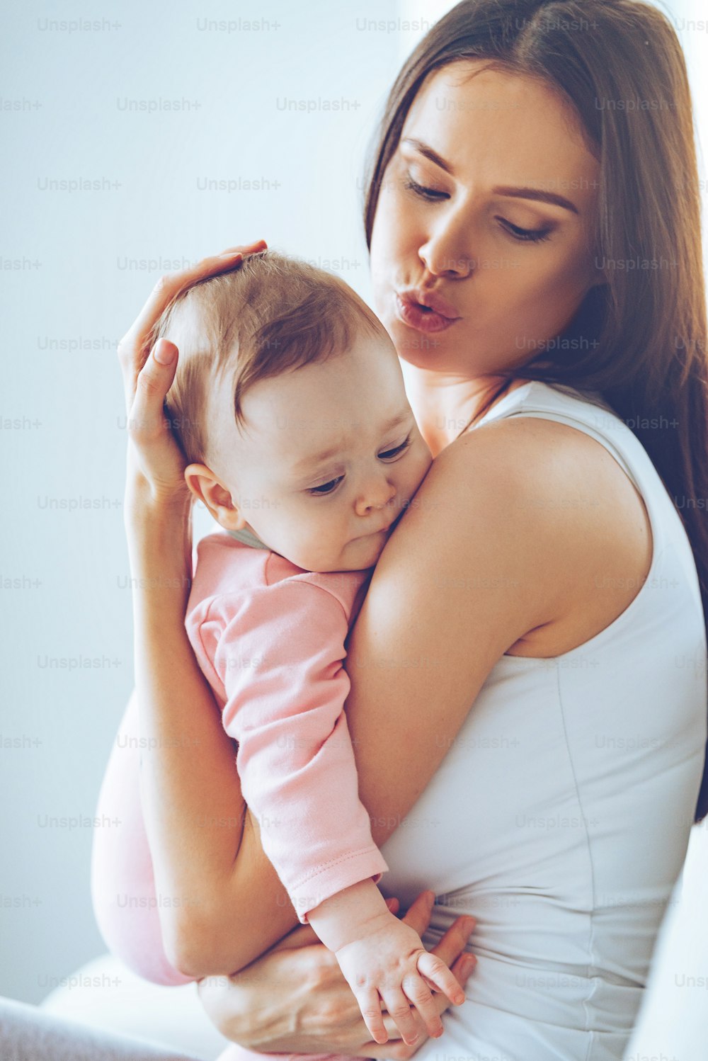 Side view of beautiful young woman calming down her baby girl while holding her in her arms at home
