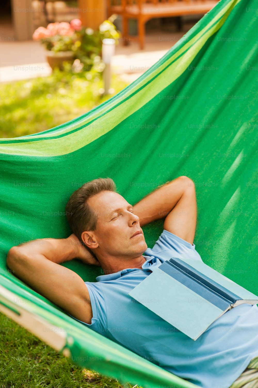 Happy mature man sleeping while lying in hammock with book laying on his torso