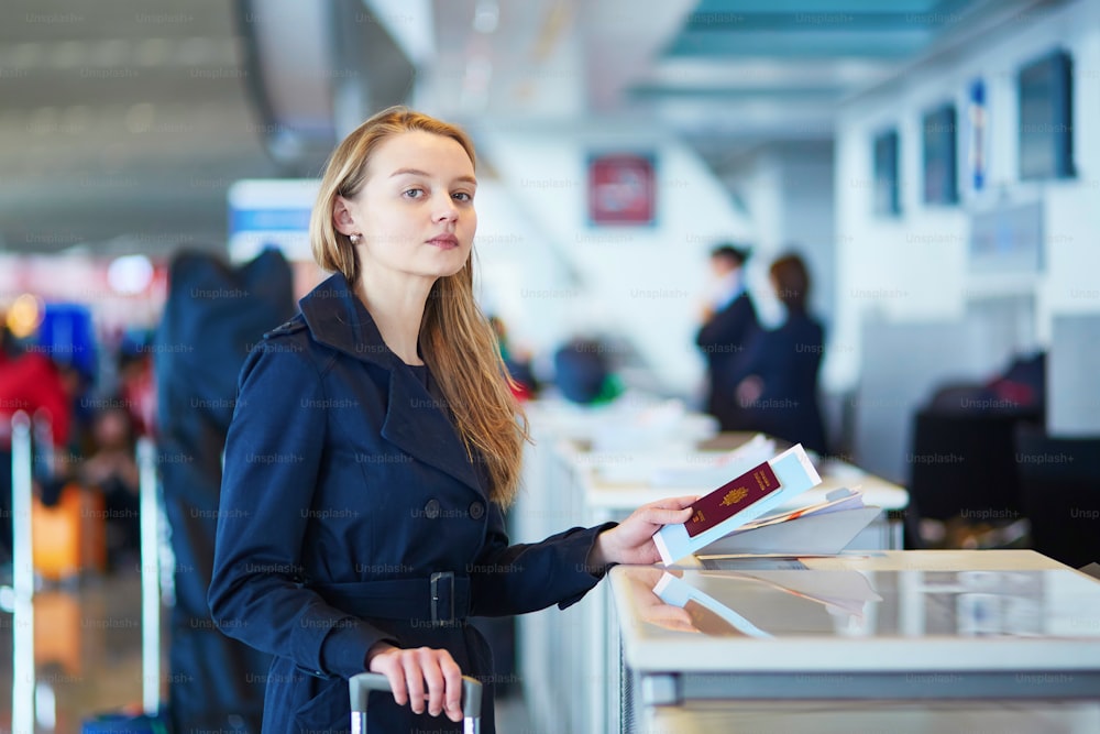 Junge Frau am internationalen Flughafen am Check-in-Schalter, die einem Beamten ihren Pass gibt und auf ihre Bordkarte wartet