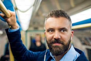 Close up of face of businessman with headphones travelling to work. Standing inside underground wagon, holding handhandle.