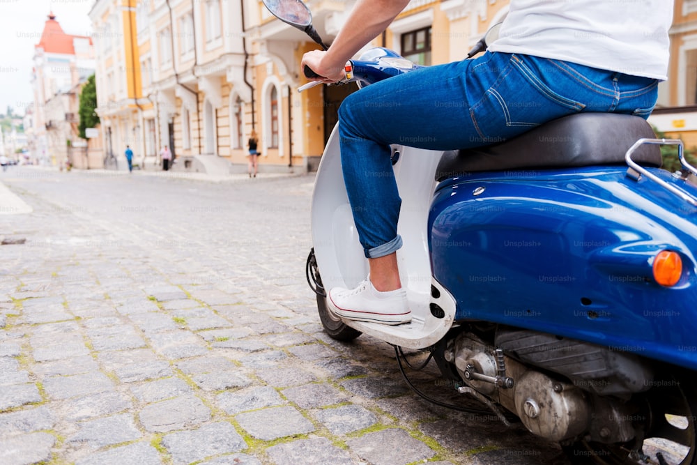 Image recadrée de vue arrière d’un jeune homme conduisant un scooter le long de la rue
