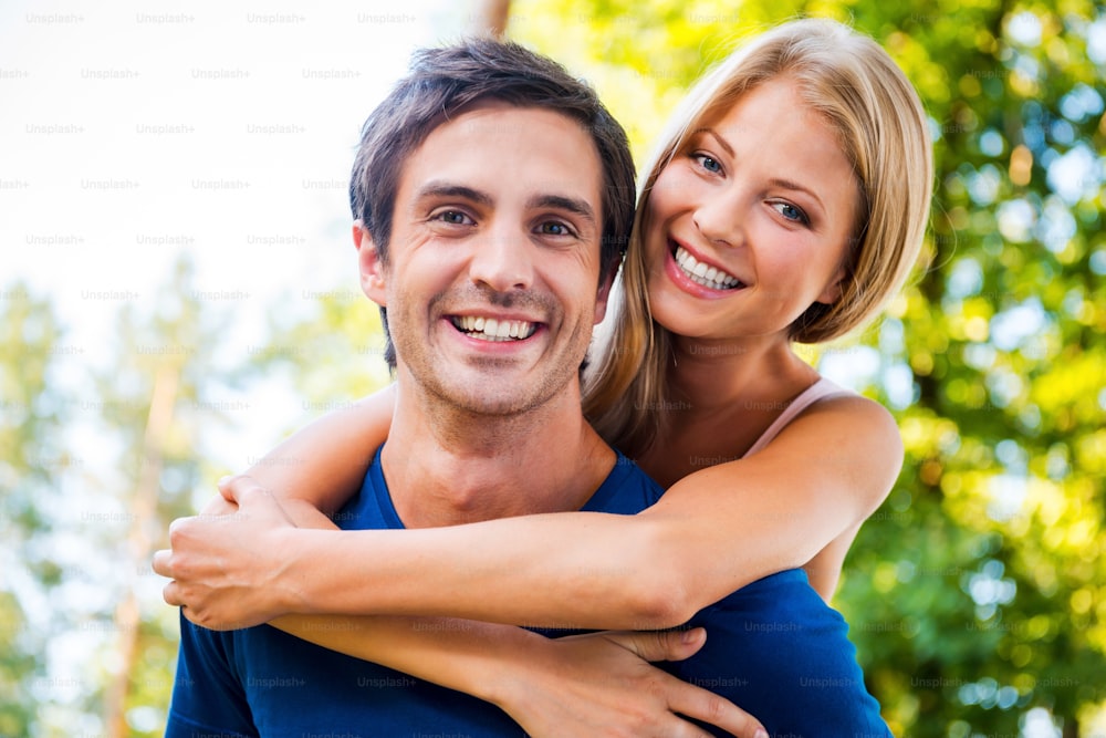 Low angle view of beautiful young loving couple standing outdoors together while woman hugging her boyfriend and smiling