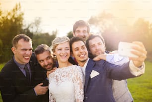 Portrait en plein air d’une belle jeune mariée avec le marié et ses amis prenant un selfie