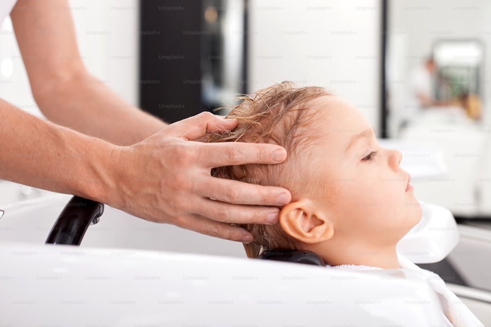 Close up of arms of cheerful hairdresser. The man is messaging head of boy during washing hair. The child is calm and relaxed