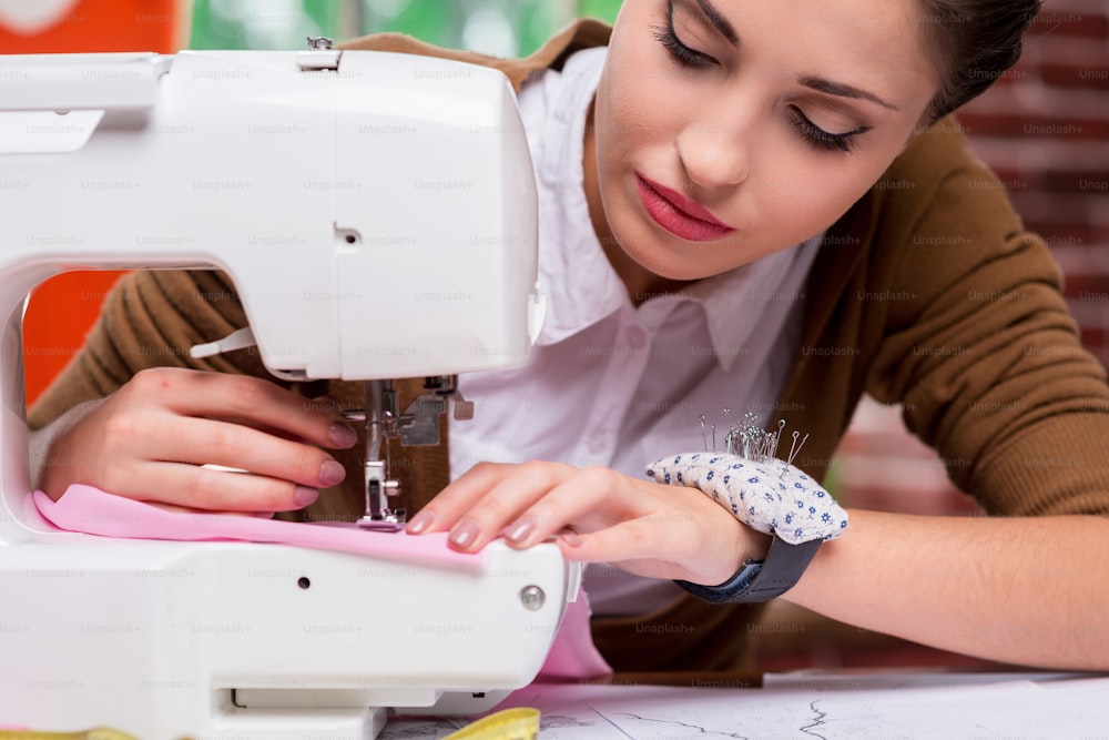 Confident female fashion designer working on sewing machine while sitting at her working place