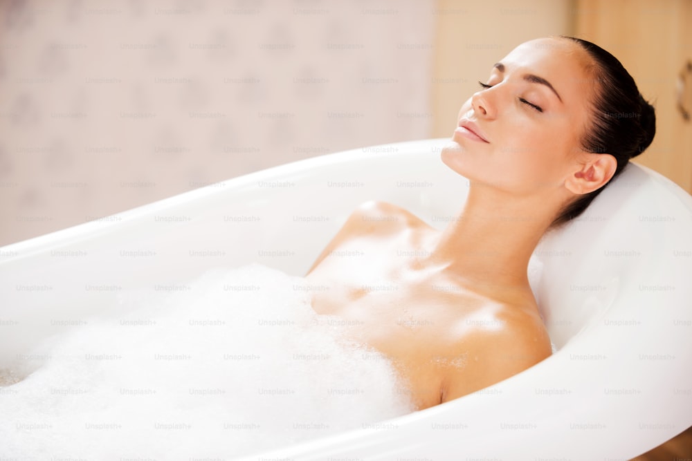 Side view of attractive young woman keeping eyes closed while enjoying luxurious bath