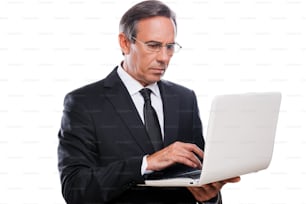 Selbstbewusster reifer Mann in formeller Kleidung, der am Laptop arbeitet, während er isoliert auf weißem Hintergrund steht