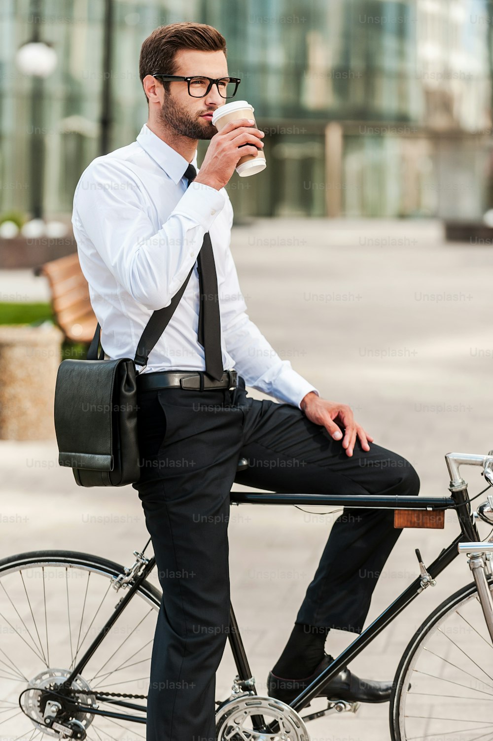 Vista lateral de un joven y guapo hombre de negocios bebiendo café mientras está sentado en su bicicleta