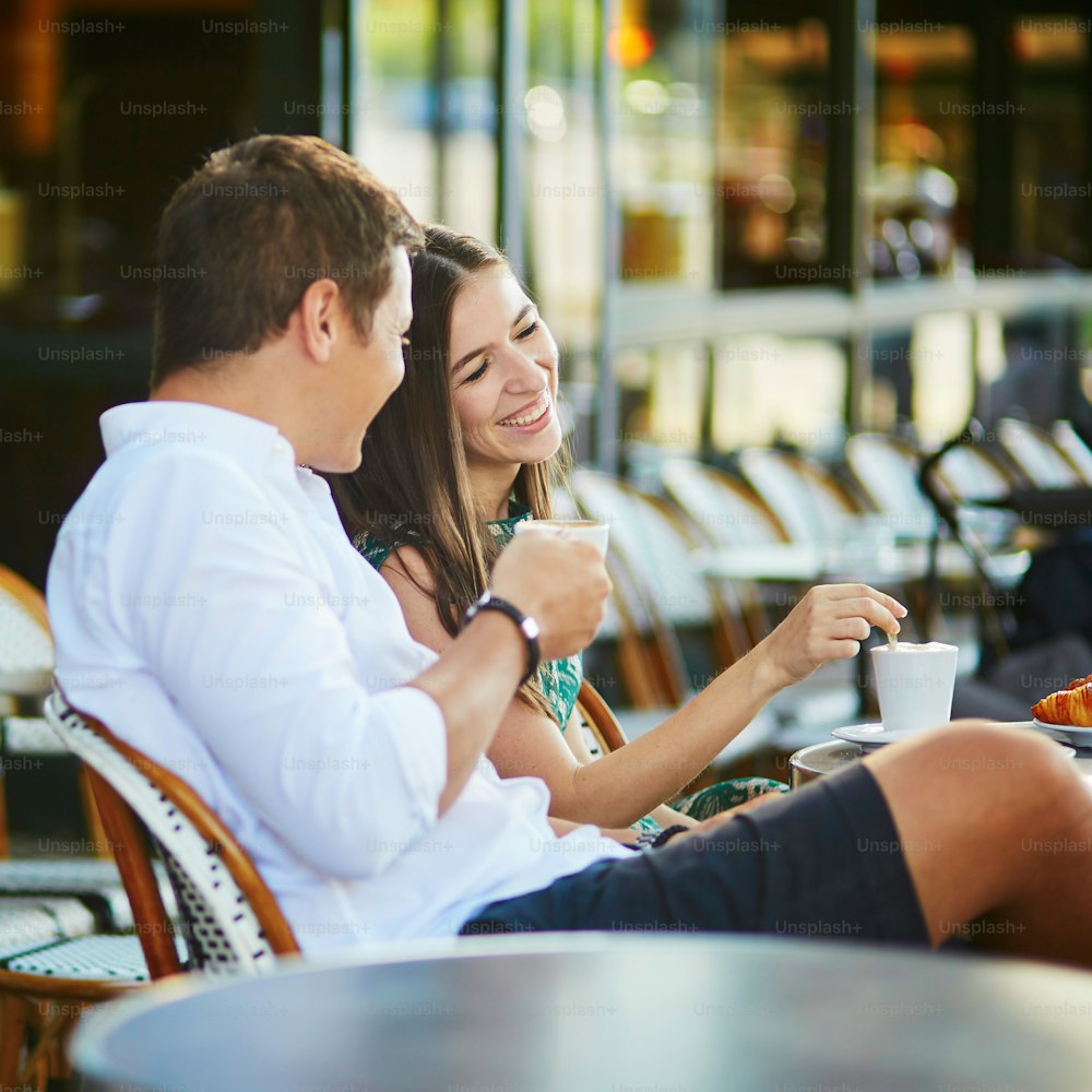 フランス・パリの居心地の良い屋外カフェでコーヒーを飲みながら伝統的なフレンチクロワッサンを食べる若いロマンチックなカップル