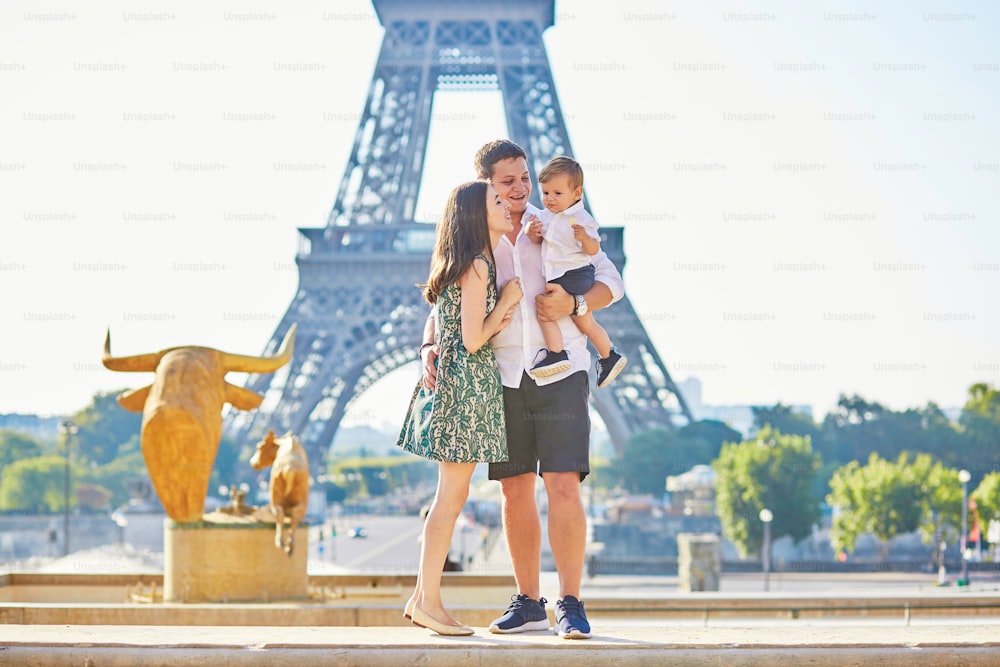 Happy family of three standing in front of the Eiffel tower and enjoying their vacation in Paris, France