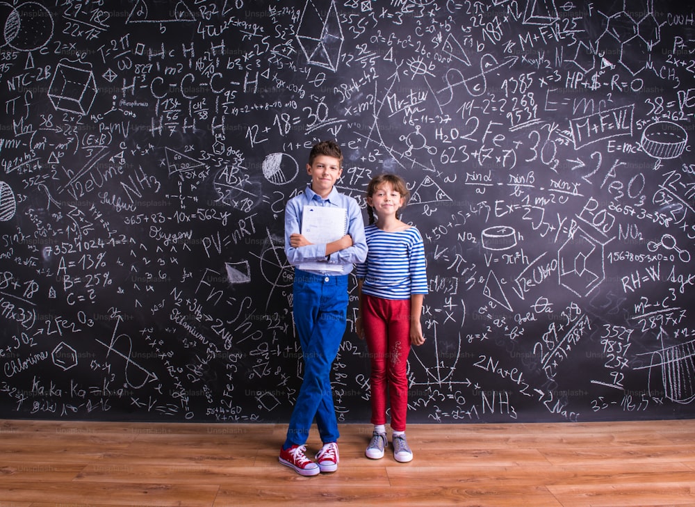 Cute little boy and girl in front of a big blackboard. Studio shot on black background.