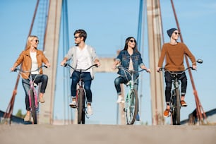 Four young people riding bicycles along the bridge and smiling