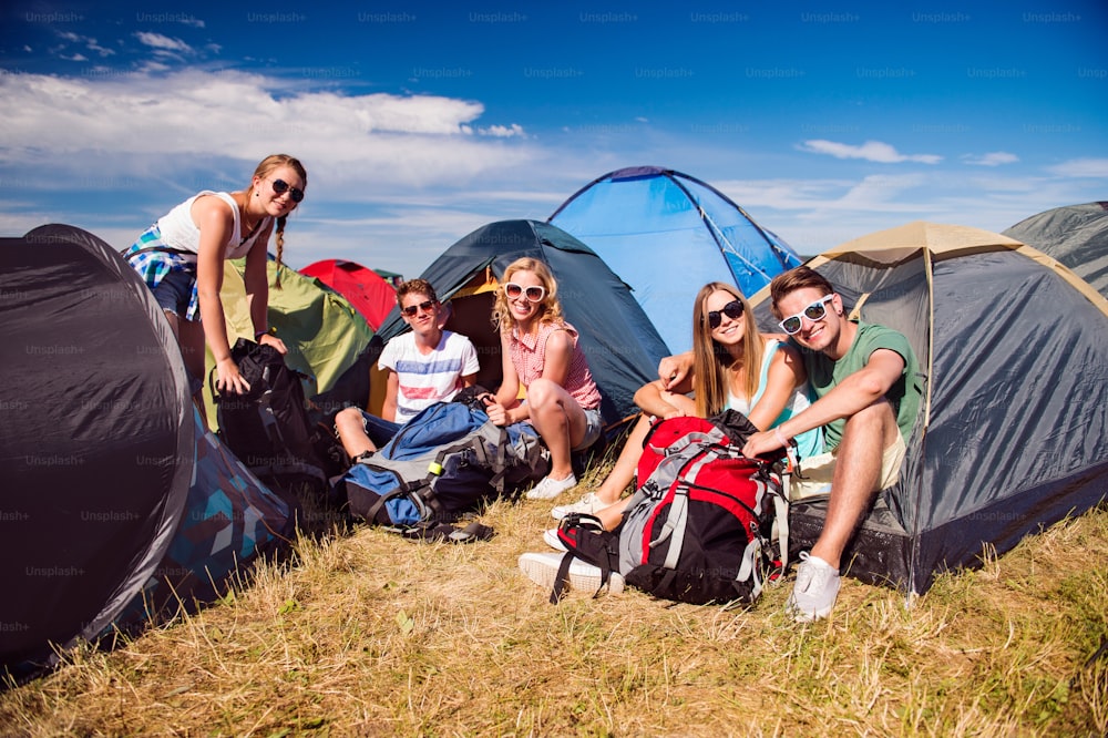 Gruppe von Teenagern beim Sommermusikfestival, auf dem Boden vor Zelten sitzend, packen