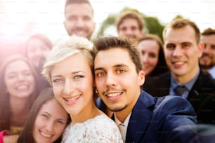 Young couple of newlyweds with group of their firends taking selfie and making funny grimaces