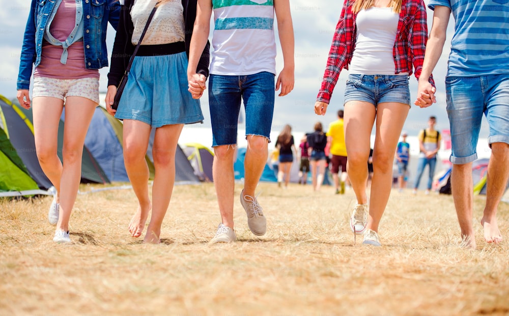 Adolescentes irreconhecíveis em tendas festival de música andando, verão ensolarado, close up de pernas