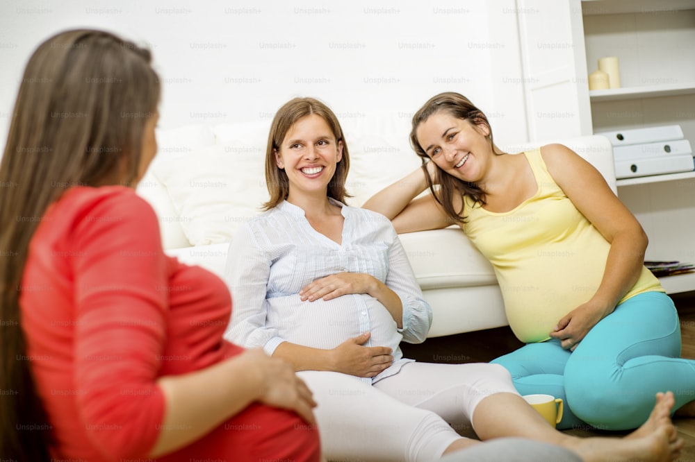 Three pregnant women sitting in front of sofa