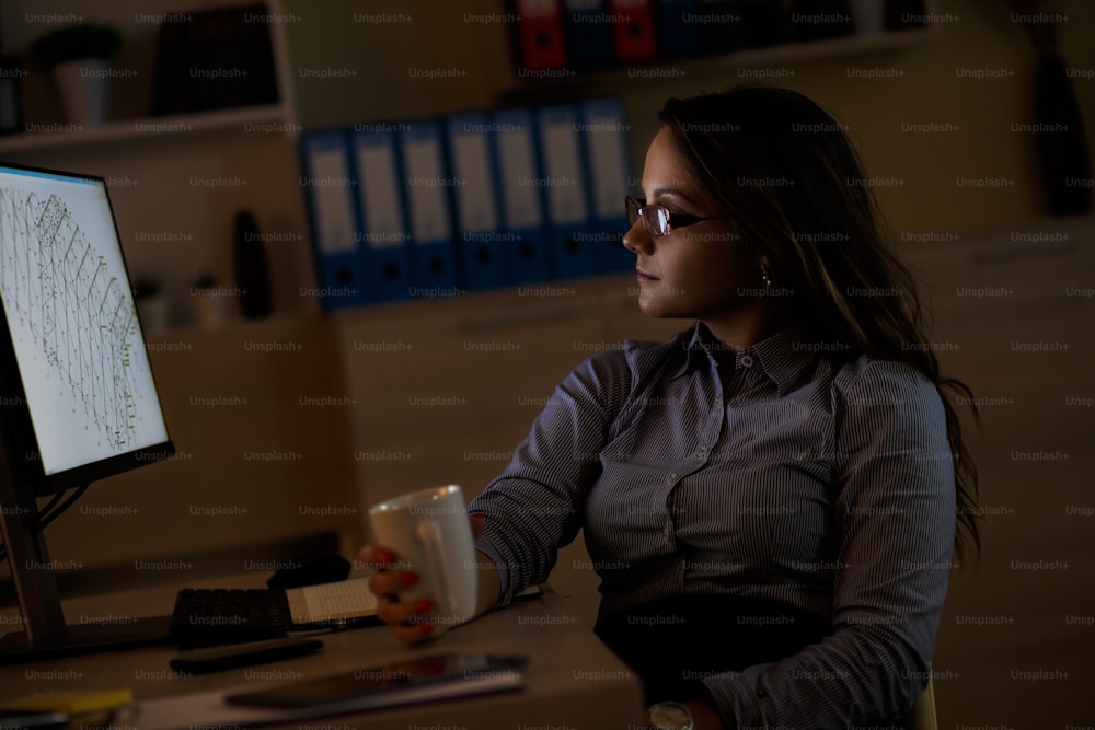 Young female business woman working at home. She takes a break and drinking coffee.