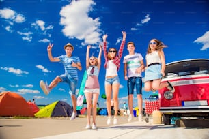 Grupo de chicos y chicas adolescentes en el festival de música de verano saltando por una autocaravana roja vintage