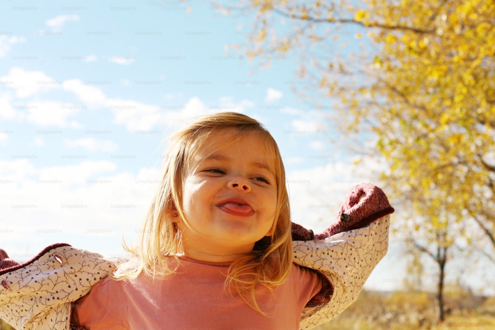 Cheerful little girl  puts out the tongue in park.