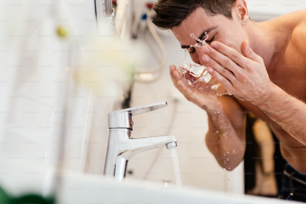 Homem bonito lavando o rosto no banheiro de manhã