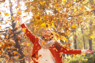 Portrait of a young woman in a park with arms outstretched. She throwing leaves in the air.