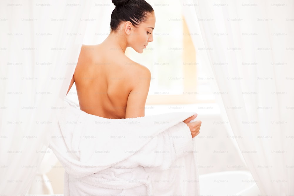 Rear view of beautiful young woman taking off her bathrobe while standing in front of bathtub
