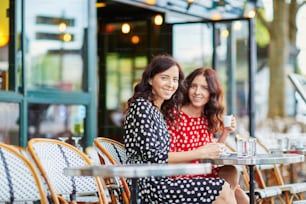 Hermosas hermanas gemelas bebiendo café en una acogedora cafetería al aire libre en París, Francia. Chicas felices y sonrientes disfrutan de sus vacaciones en Europa