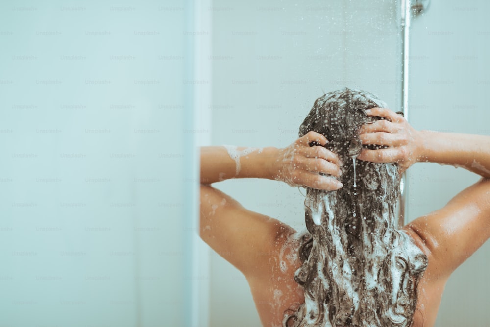Junge Frau wäscht Kopf mit Shampoo. Rückansicht