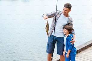 Vater hält Angelrute und zeigt seinem Sohn große Fische