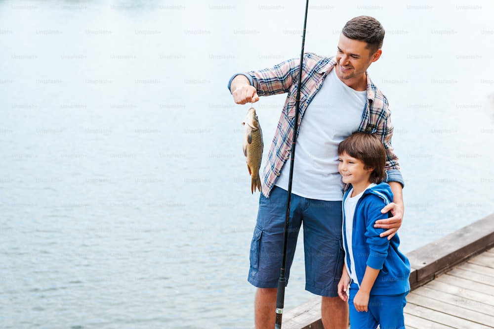Father holding fishing rod and showing big fish to his son