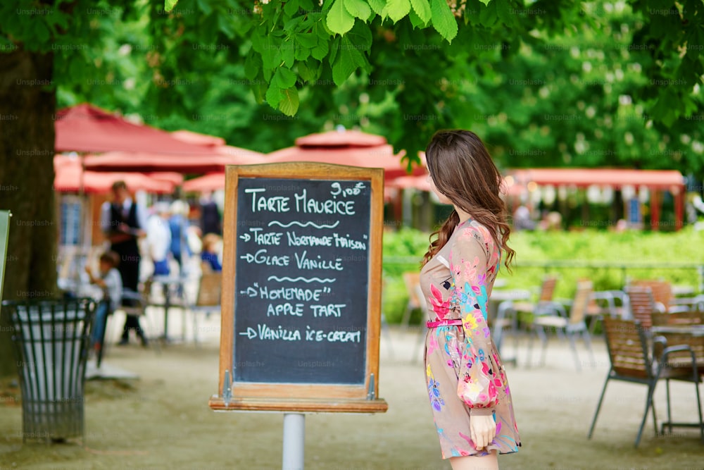 Bella giovane donna parigina che legge il menu scritto a mano nel ristorante parigino nel giardino delle Tuileries in una soleggiata giornata estiva