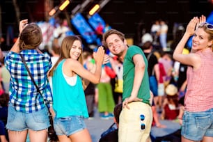 Teenagers at summer music festival against the stage in a crowd enjoying themselves, clapping and singing