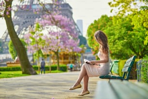晴れた春の日、パリのエッフェル塔の近くで、屋外のベンチで読書をしている美しい若い女性