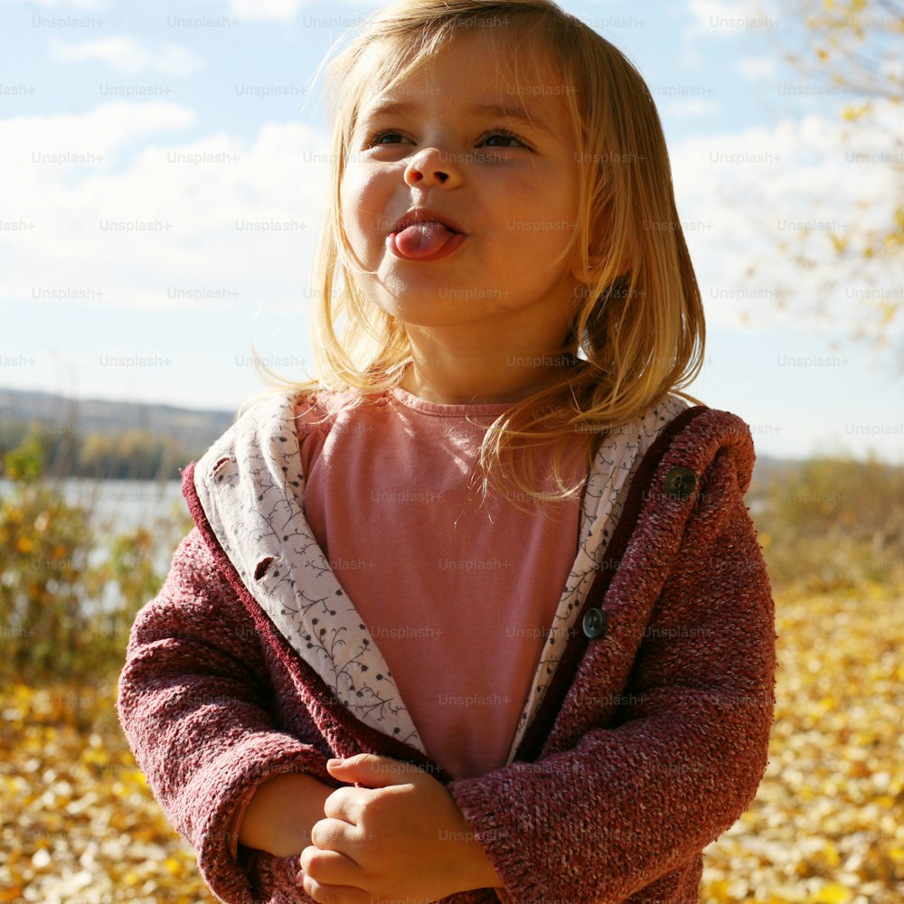 Cheerful little girl  puts out the tongue in park.