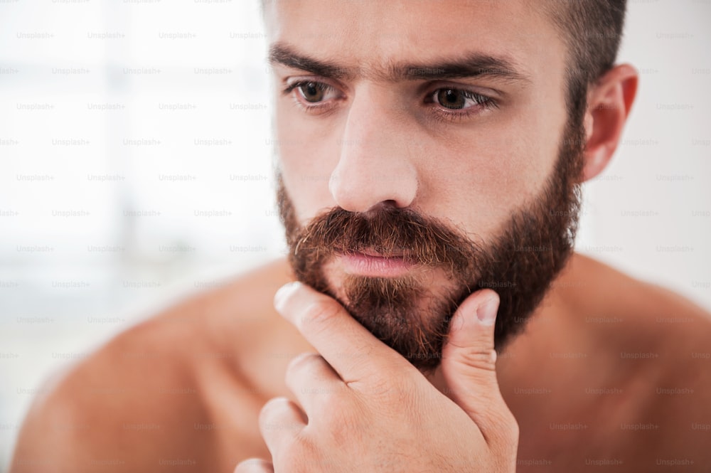 Portrait of thoughtful young bearded man holding hand on chin and looking away