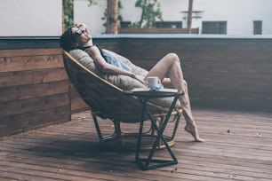 Beautiful young woman relaxing in a big comfortable chair on her outdoor house terrace