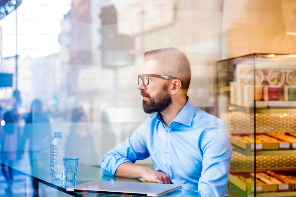Hipster manager sitting in cafe by the window with glass of water and notebook, reflection