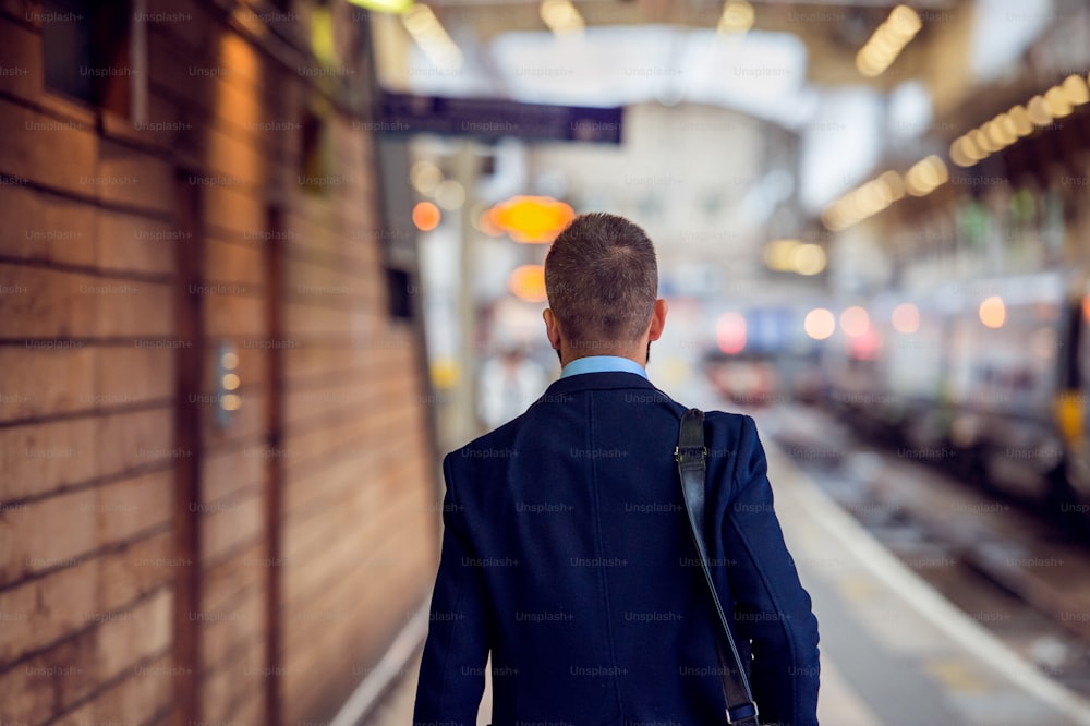 Businessman in suit walking at the train staition platform, back view, rear viewpoint